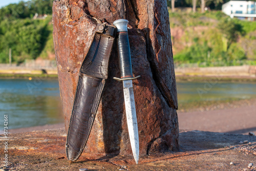 Foto Commando dagger with a leather sheath leans against a rusty post on a beach