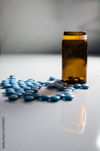 glass medicine bottle, blue pills on white table with gray background 