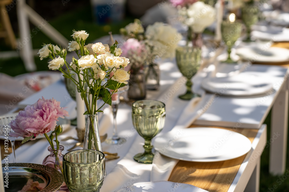 Wooden table outdoors for a special occasion. Empty plates and unusual glasses. Vintage tray, candleholder and vases with beautiful flowers.