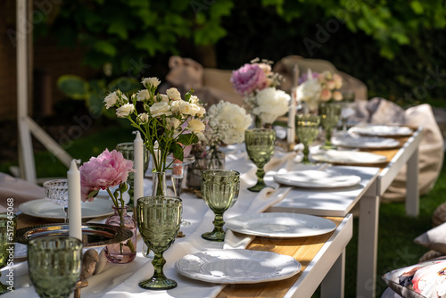 The table is set for special occasions. Empty plates and unusual glasses. vintage tray, candle holder and vases with beautiful flowers. Everything for a special day