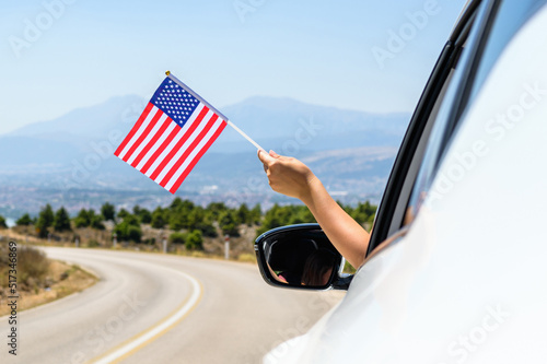 Woman holding USA flag from the open car window driving along the serpentine road in the mountains. Concept