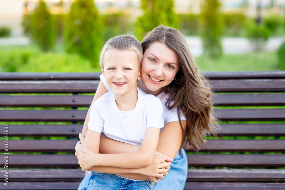 Naklejka premium happy mom and her baby son in the park on a bench in the summer have fun hugging, laughing and playing