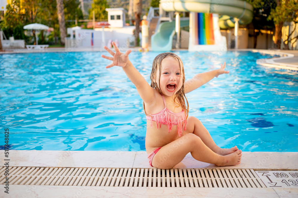 happy baby girl at the pool with water slides shouts hooray and laughs having fun on vacation, raising her hands up, the concept of recreation and travel