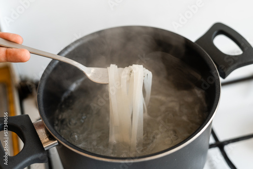 Fork with rice noodles and pan with boiling water on the kitchen. Cooking asian food 