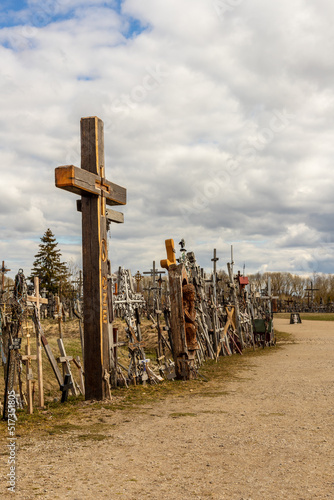 Vertical photo of hill of crosses near Šiauliai, Lithuania in cloudy spring day. Wooden Catholic crosses at path side. Religious pilgrimate place in Lithuania, Europe.  photo