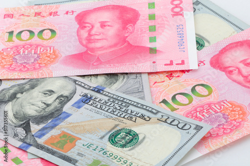 Chinese 100 Renminbi and 100 U.S. dollar bills piled on a white background.