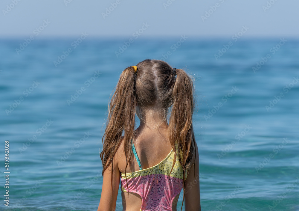 A little girl in a bathing suit looks at the sea.