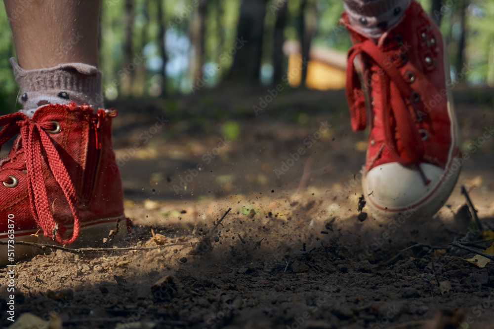 A man in red sneakers runs on the ground in a forest park. Forest, a place to relax and play sports. From under the sole flies dust and dirt close-up. Typing soft focus A man in red sneakers runs on the ground in a forest park. Forest, a place to relax and play sports. From under the sole flies dust and dirt close-up. Typing soft focus