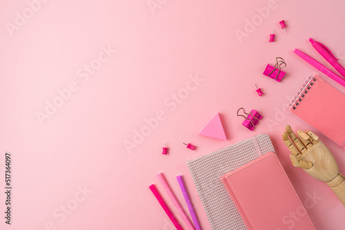 Feminine desk workplace with notebook, wooden hand and pens on pink background. Back to school concept. Top view, flat lay