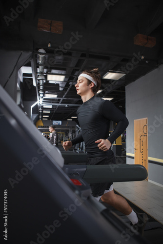Vertical shot of a handsome athletic man running on treadmill at the gym