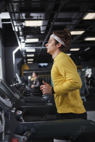 Vertical profile shot of a male athlete wearing headband, running on treadmill at gym © Ihor