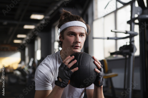 Focused male athlete wearing headband, exercising with medicine ball