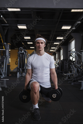 Vertical full length shot of a male athlete doing lunges with dumbbells