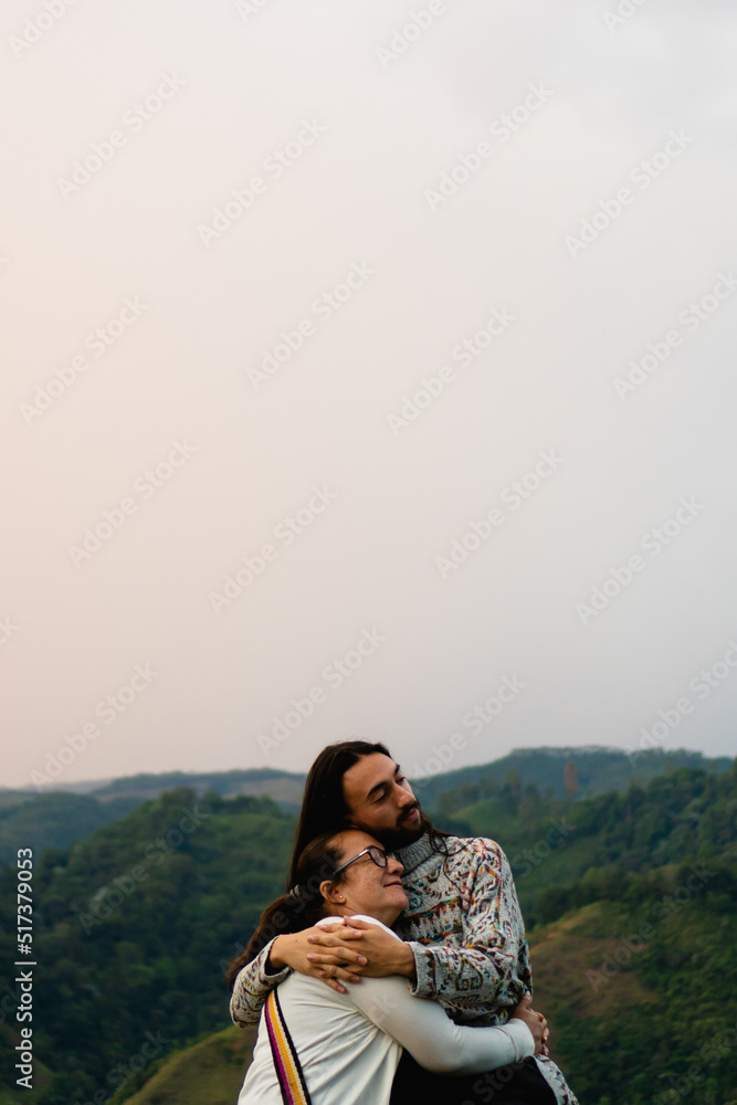latin mother and son hugging tourists, mountain landscape background in colombia. vertical photo with copy space
