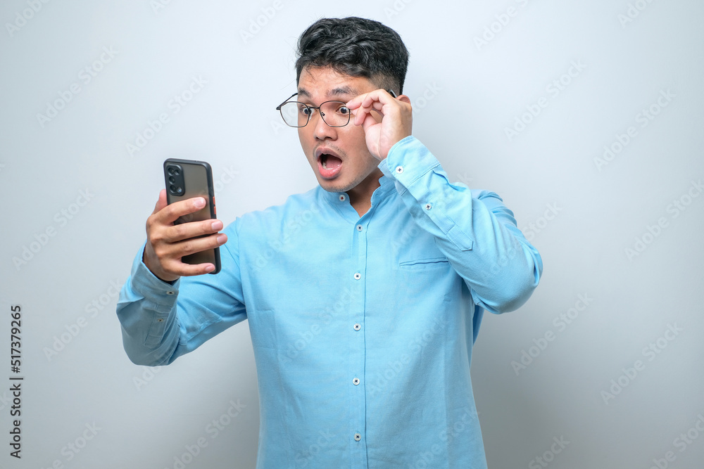Shocked young good looking Asian man using smartphone to read good news online isolated Shocked young good looking Asian man using smartphone to read good news online isolated