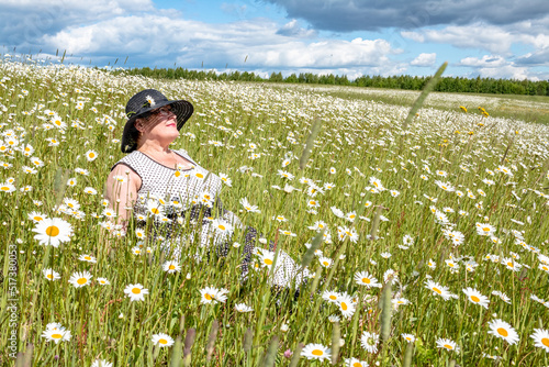 An elderly woman is resting in a field of daisies.
