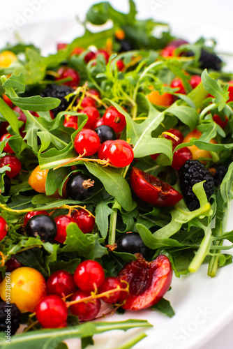 Summer delicious salad with arugula and fresh berries, red and black currants, sweet cherries and black mulberries, salad in an oval plate on a white background