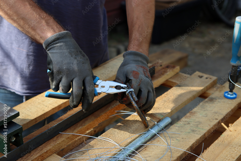 Man holds pliers and steel wire. Handyman tools close up photo. Male hands in grey protective gloves. 