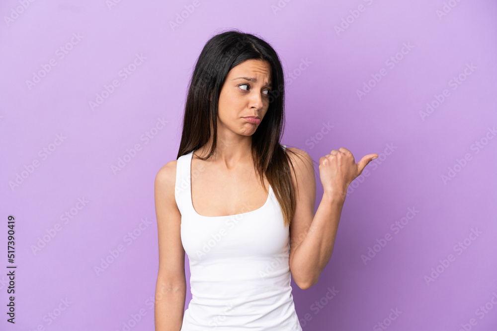Young caucasian woman isolated on purple background unhappy and pointing to the side Young caucasian woman isolated on purple background unhappy and pointing to the side
