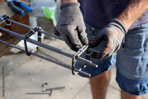 Professional builder works with reinforcement steel. Construction work in process. Man in grey gloves holds metal framework. 