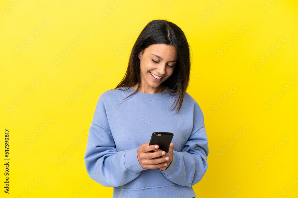 Young caucasian woman isolated on yellow background sending a message with the mobile Young caucasian woman isolated on yellow background sending a message with the mobile