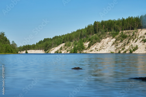 Blue lake and green mixed forest on a sunny summer day. Girvas paleovolcano is popular place among tourists. The concept of travel in Russia. Blurred surface of water is long exposure. © Ekaterina