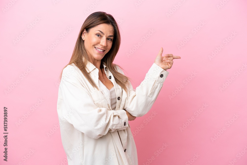 Middle age caucasian woman isolated on pink background pointing finger to the side Middle age caucasian woman isolated on pink background pointing finger to the side