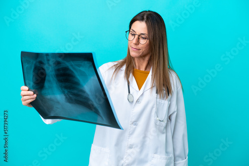 Middle age woman isolated on blue background wearing a doctor gown and holding a bone scan