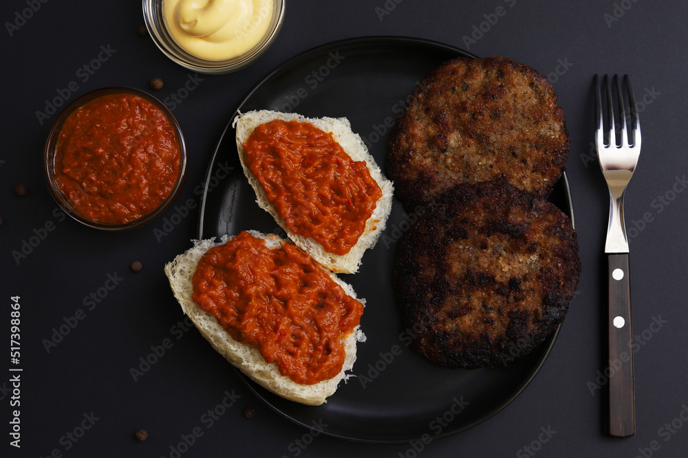 Cutlets with eggplant caviar sandwiches on a black plate under dark lighting. Shallow depth of field