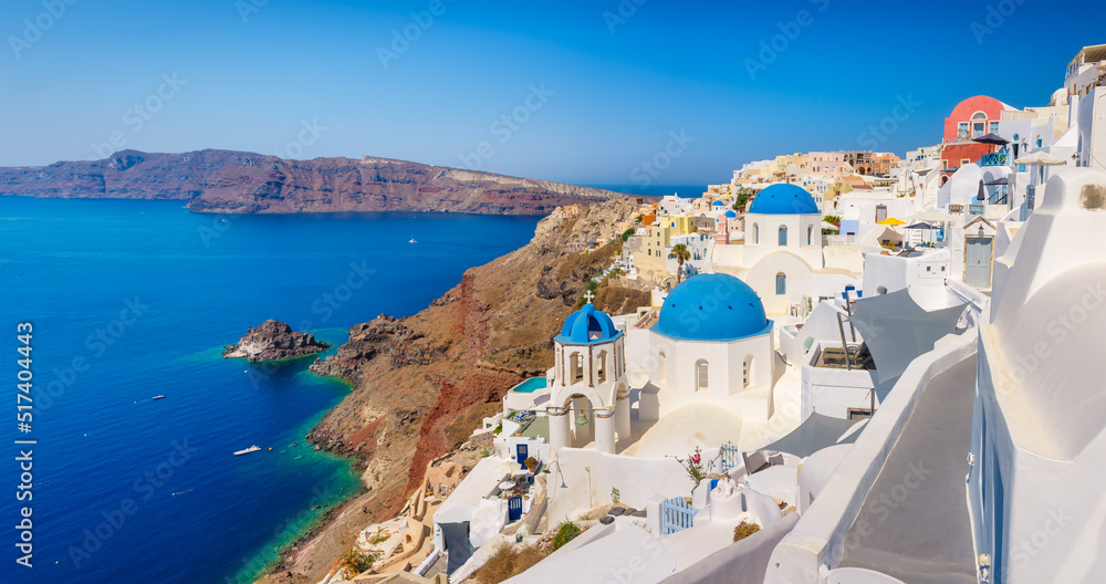 Fototapeta premium Santorini, Greece. Panoramic view of traditional houses in Santorini. Small narrow streets and rooftops of houses, churches and hotels. Oia village, Santorini Island, Greece.