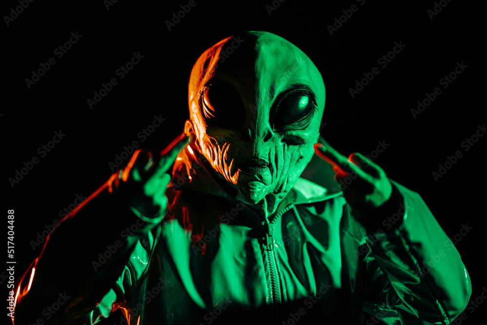 Alien showing middle finger - gesture of fuck. Expression negative, aggression, provocation. Creepy mask of humanoid on neon planet in smooth raincoat. UFO, fiction concept. Alien showing middle finger - gesture of fuck. Expression negative, aggression, provocation. Creepy mask of humanoid on neon planet in smooth raincoat. UFO, fiction concept.