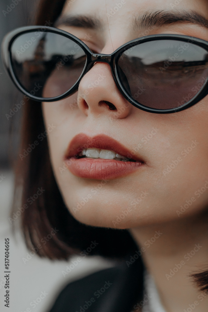 a brunette girl in a black jacket and dress and black glasses sits in the city with a handbag a brunette girl in a black jacket and dress and black glasses sits in the city with a handbag