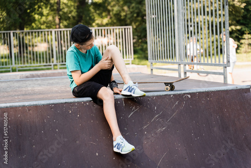 Active child boy after fall from skate board injured, sitting and looking at bruise on sport ramp on skate park playground. © Rabizo Anatolii