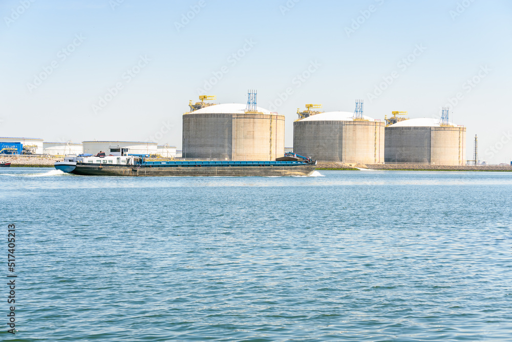 Bulk carrier barge in harbour with large concrete tanks for storage of liquefied natuaral gas in background. Port of Rotterdam, Netherlands.