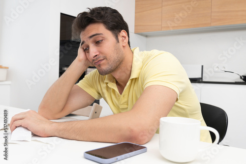 Close up of unhappy man sitting at the table, stressed and confused by calculate expense from invoice or bills, have no money to pay mortgage or loan. High prices and spending money concept