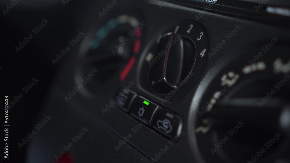 The woman turns on the fan and presses the air conditioner button in the car. Automotive panel close-up.