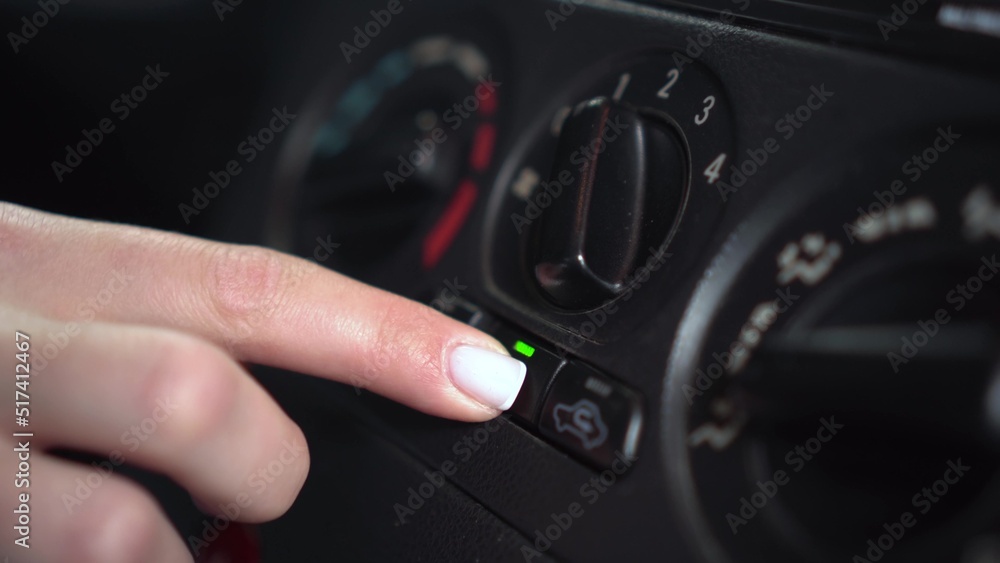 The woman presses the air conditioner button in the car. Automotive panel close-up.