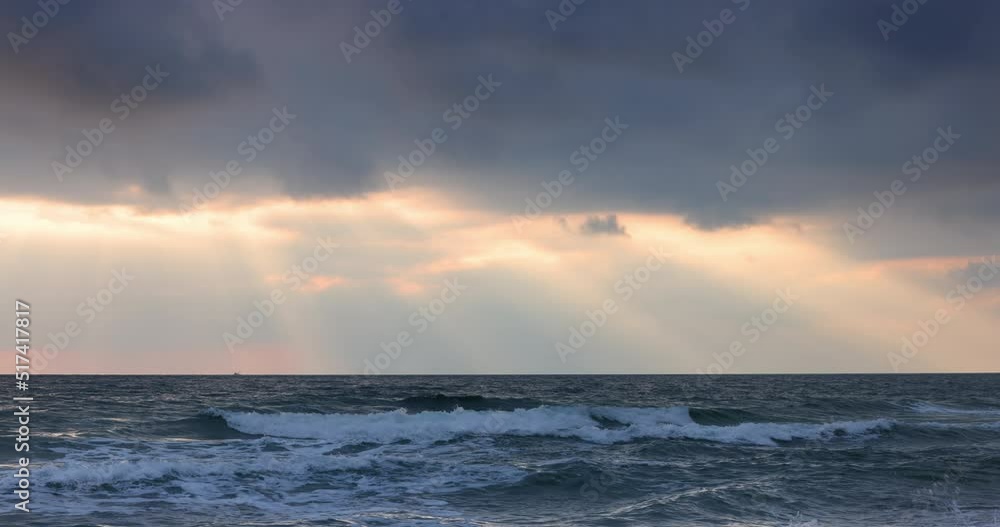 Ocean beach sunrise with dark sky clouds and sun rays over sea waves Ocean beach sunrise with dark sky clouds and sun rays over sea waves