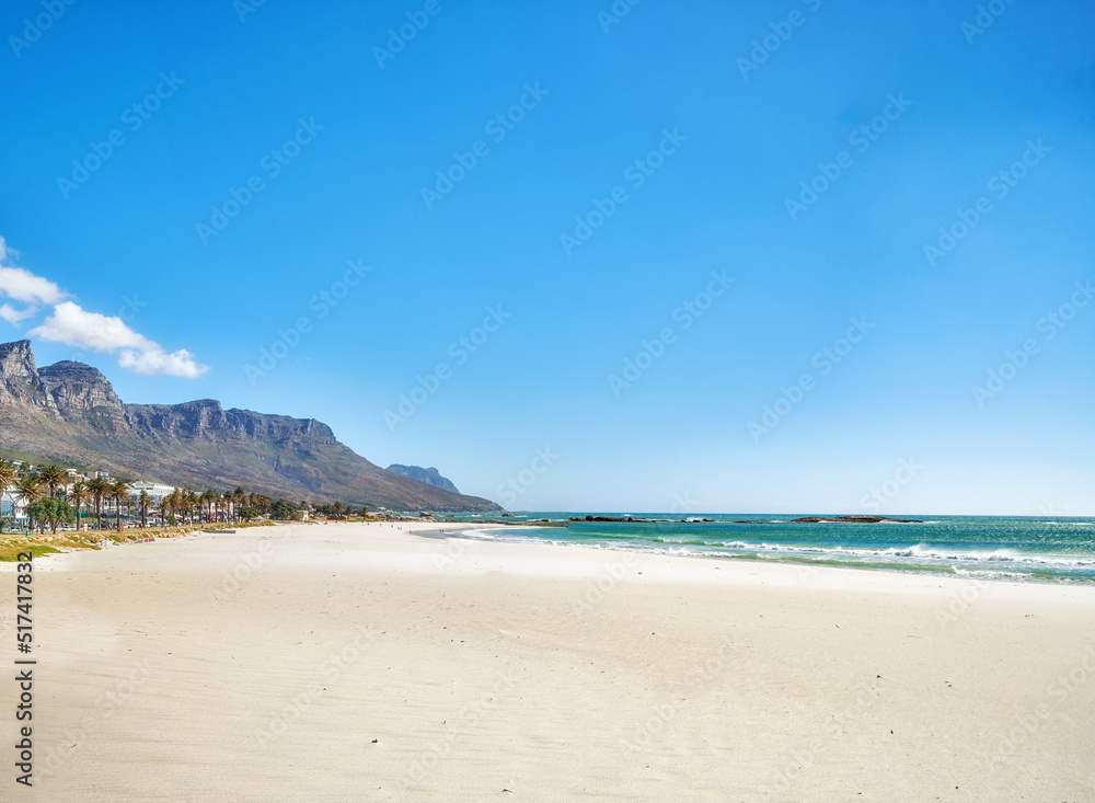 Copy space at sea with a clear blue sky and mountain in the background. Calm ocean waters washing onto an empty beach shore. Peaceful scenic coastal landscape for a relaxing and zen summer getaway
