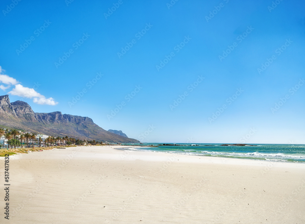 Copy space at sea with a clear blue sky and mountain in the background. Calm ocean waters washing onto an empty beach shore. Peaceful scenic coastal landscape for a relaxing and zen summer getaway Copy space at sea with a clear blue sky and mountain in the background. Calm ocean waters washing onto an empty beach shore. Peaceful scenic coastal landscape for a relaxing and zen summer getaway