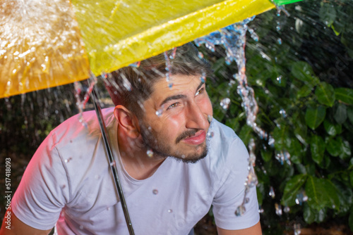 image amusante d'un jeune homme sous un parapluie. Il est sous un orage et il pleut beaucoup. Il fait des grimaces car il est mouillé photo