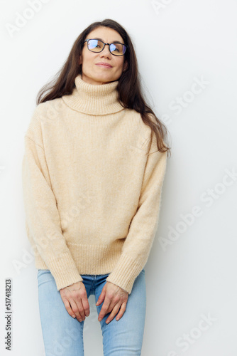 beautiful cute happy woman in a beige warm sweater with a high neck stands in glasses and light jeans on a white background.