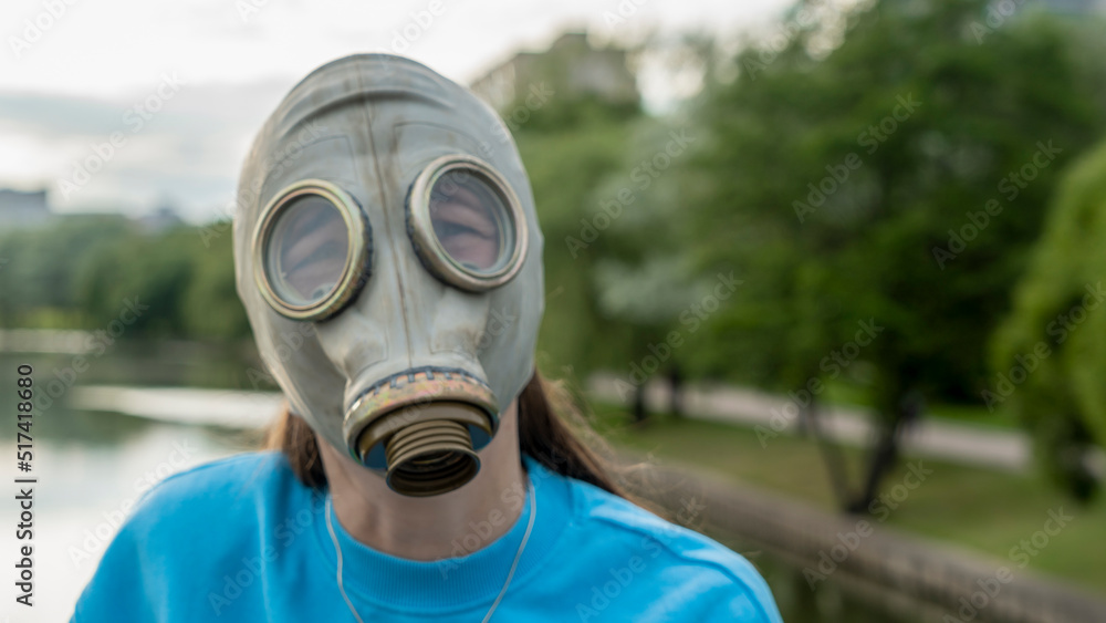 A girl in a gas mask stands on a bridge across the river. Alienation in the city. Fashion, ecology and loneliness concepts. A girl in a gas mask stands on a bridge across the river. Alienation in the city. Fashion, ecology and loneliness concepts.
