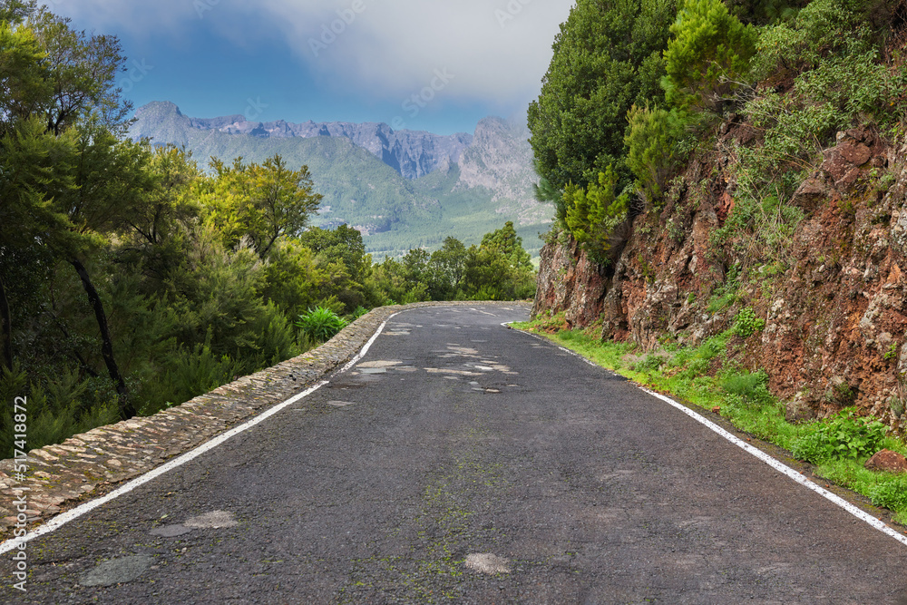 Empty road on the mountains with a cloudy blue sky. Landscape of a countryside roadway for traveling on a mountain pass along a beautiful scenic nature drive with green trees and mountain views