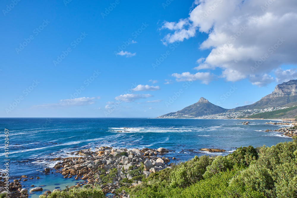 A nature scenery of a calm sea and green bushes, with Lions Head mountain in the horizon, Cape Town, South Africa. Landscape of the ocean near the mountains with blue cloud sky and copy space. A nature scenery of a calm sea and green bushes, with Lions Head mountain in the horizon, Cape Town, South Africa. Landscape of the ocean near the mountains with blue cloud sky and copy space.