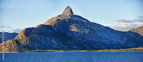 Scenic view a mountain lining a coast in Bodo, Norway. An expansive natural vista of a spring lake during sunrise in the morning. Remote, lush vegetation alongside a lake in a European destination