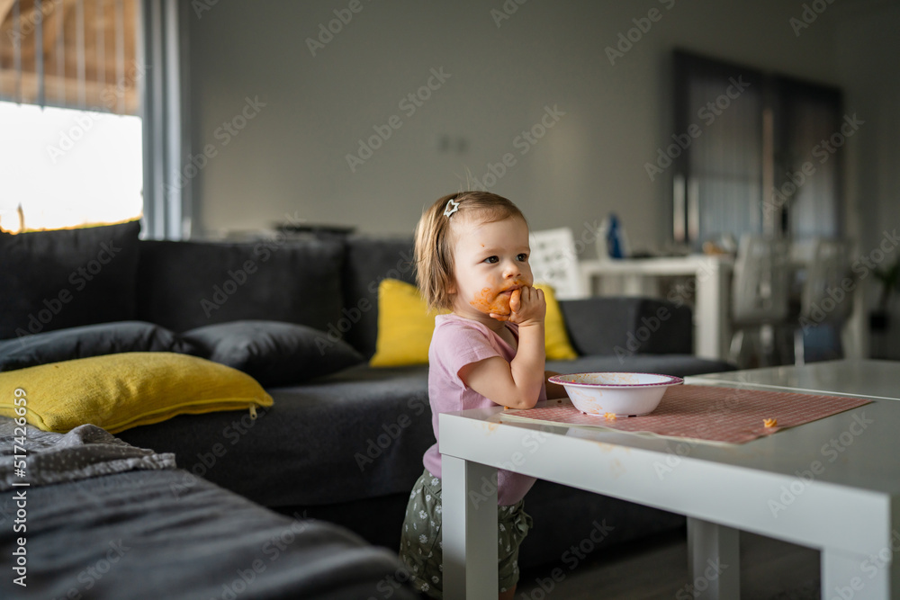 one girl small caucasian toddler female child daughter eating alone at the table at home while watching tv making mess on her face dirty sauce childhood growing up development concept copy space one girl small caucasian toddler female child daughter eating alone at the table at home while watching tv making mess on her face dirty sauce childhood growing up development concept copy space