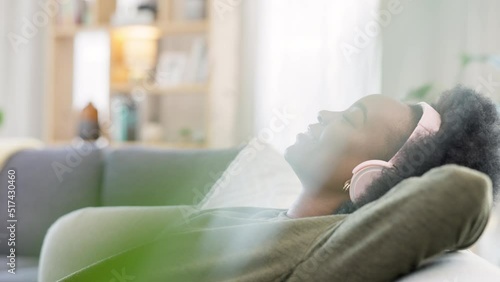 Young woman listening to music while relaxing on a sofa at home. Carefree, cheerful and happy female wearing headphones while enjoying a podcast and favourite songs. Taking a break to rest in comfort photo