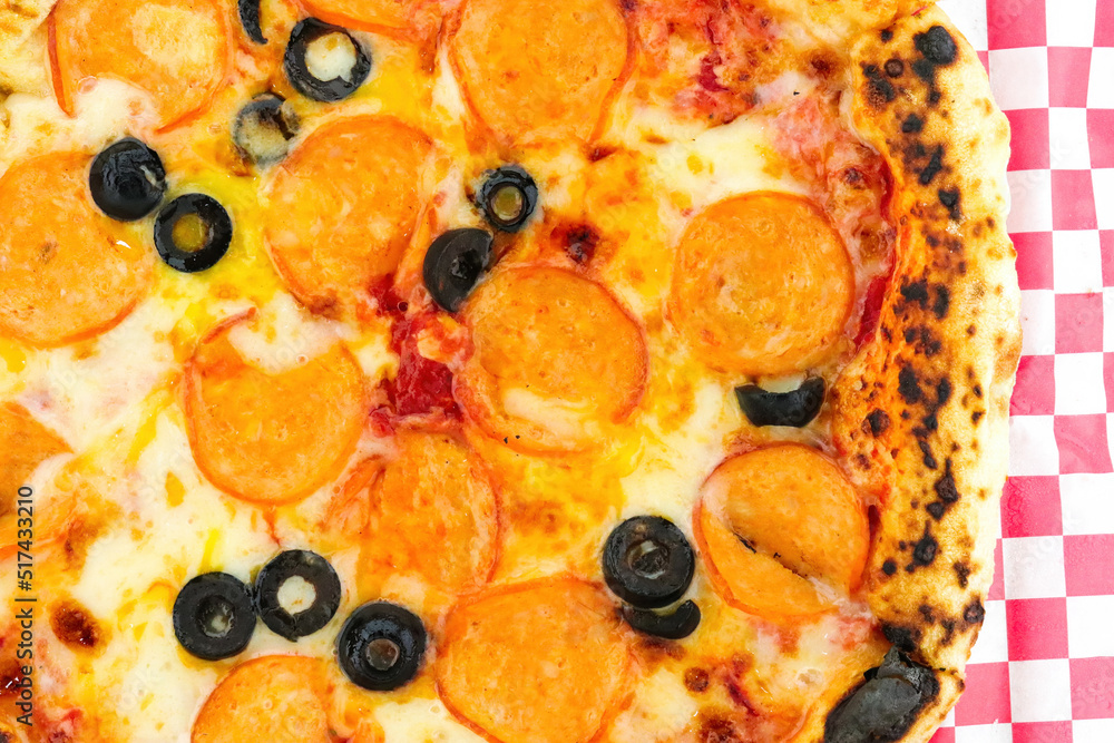 Chicken pepperoni pizza with black olives on red checkered paper Chicken pepperoni pizza with black olives on red checkered paper