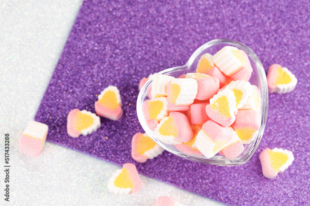 Colorful miniature marshmallows in a love shape glass on a purple white background